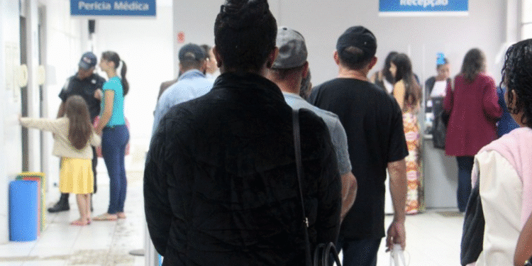Pessoas em fila aguardando atendimento na recepção da perícia médica em ambiente interno.