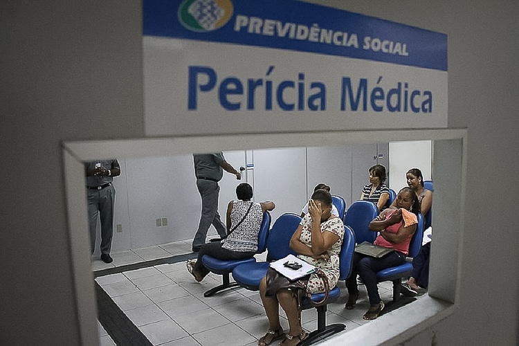 Pessoas aguardam atendimento em sala de espera para perícia médica do INSS.