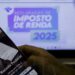 Pessoa acessando o site da Receita Federal pelo celular com tela ao fundo sobre a Declaração do Imposto de Renda 2025.