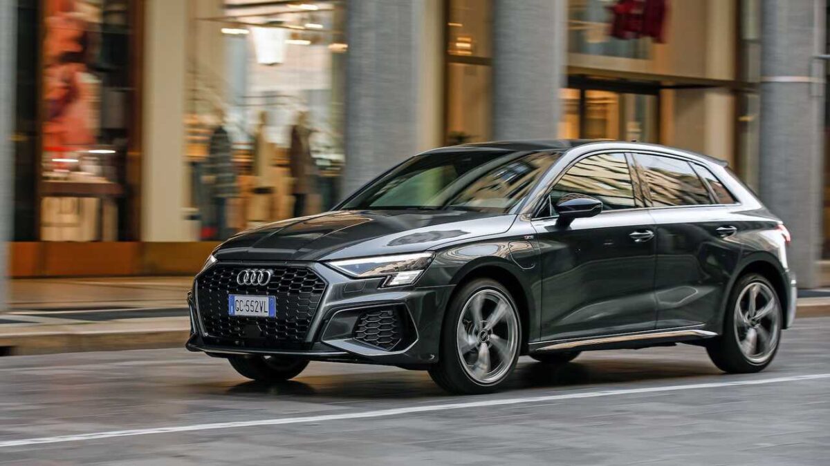 Audi A3 Sportback cinza escuro (nova geração), em movimento em ambiente urbano com lojas ao fundo, simbolizando a compra de um carro premium usado.