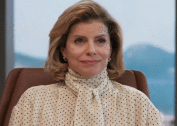 Mulher loira de cabelo curto vestindo blusa branca com poás pretos sentada em cadeira de escritório