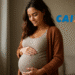 Gestante sorrindo, com as mãos sobre a barriga, confirmando o pagamento extra da CAIXA para gestantes.