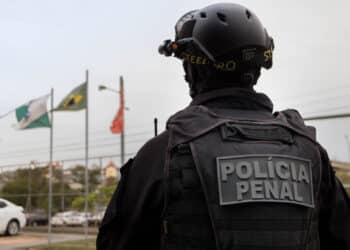 Agente da polícia penal usando colete tático preto e capacete com acessórios de visão noturna.