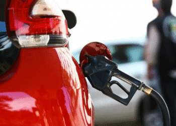 Carro vermelho sendo abastecido com bomba de combustível preta em posto de gasolina