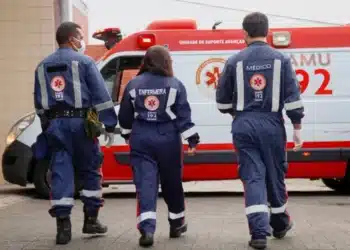 Trio de profissionais do SAMU uniformizados de costas caminhando em direção à ambulância vermelha durante plantão