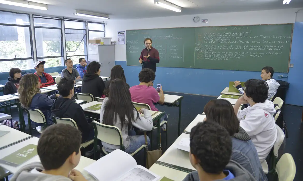 Aula com professor explicando para alunos em sala de aula Professor ensinando alunos em classe com quadro negro cheio de anotações ao fundo