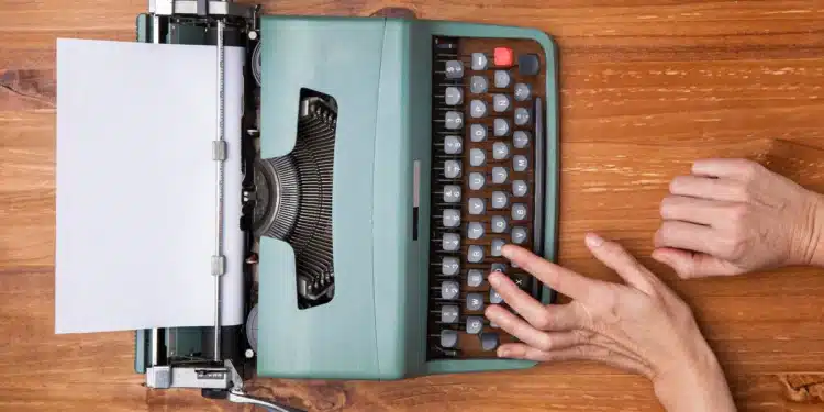 Máquina de escrever antiga com uma folha em branco e mãos digitando, simbolizando profissões do passado.