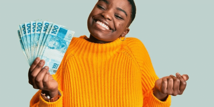 Mulher sorridente vestindo suéter amarelo segurando várias notas de 100 reais.