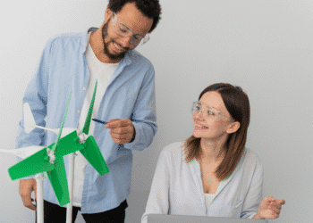 Dois jovens engenheiros com óculos de proteção ajustando modelos de turbinas eólicas verdes em laboratório.