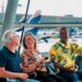 Grupo de três idosos sorrindo enquanto esperam no aeroporto com aviões ao fundo