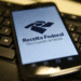 Smartphone mostrando o aplicativo Meu Imposto de Renda da Receita Federal sobre teclado de computador.