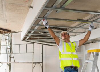 Trabalhador de construção civil ajustando estrutura de teto durante obra, com colete de segurança e capacete, ilustrando o Programa Reforma Casa Brasil.