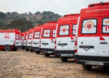 Várias ambulâncias SAMU 192 alinhadas em um terreno com paisagem de árvores e colinas ao fundo