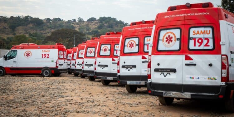 Várias ambulâncias SAMU 192 alinhadas em um terreno com paisagem de árvores e colinas ao fundo