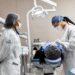 Duas dentistas com avental branco e máscaras atendendo paciente em cadeira odontológica profissional