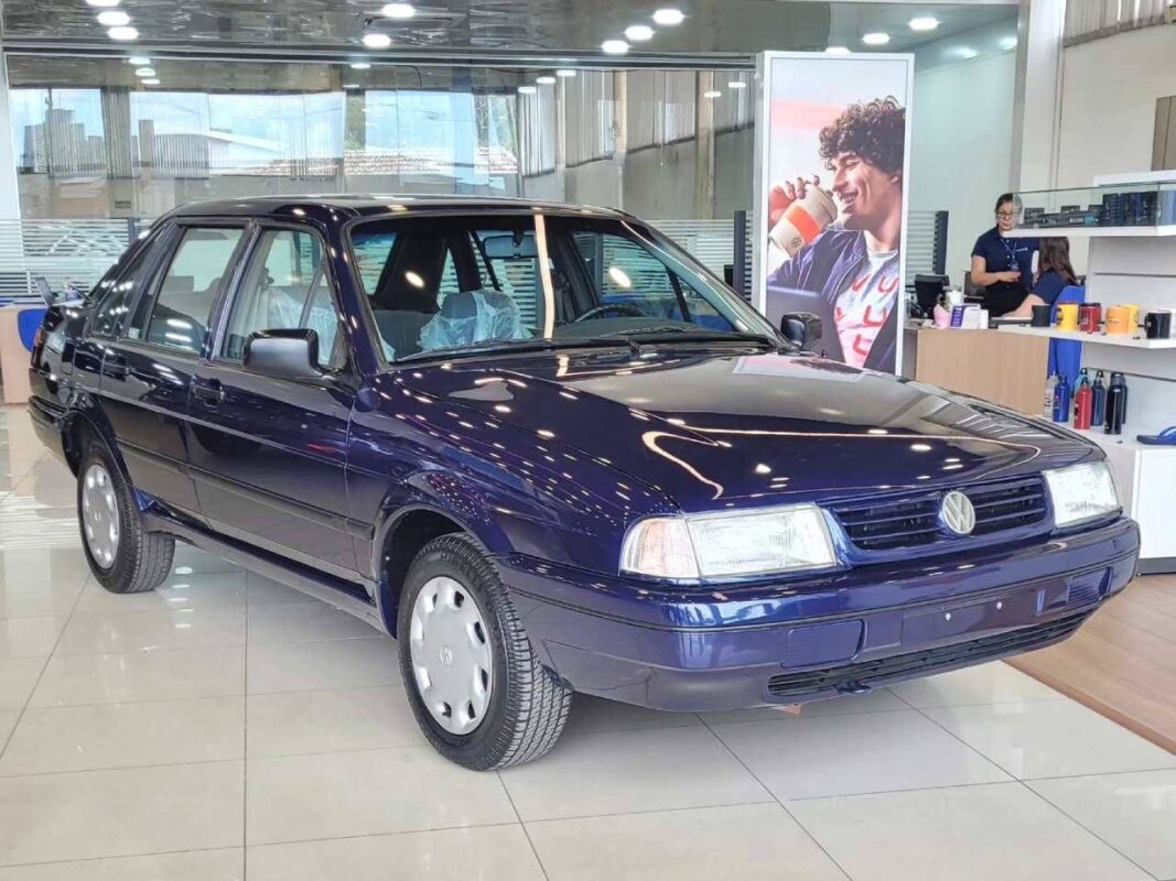 Carro Volkswagen Santana azul escuro estacionado em showroom com ambiente iluminado e reflexos no vidro.