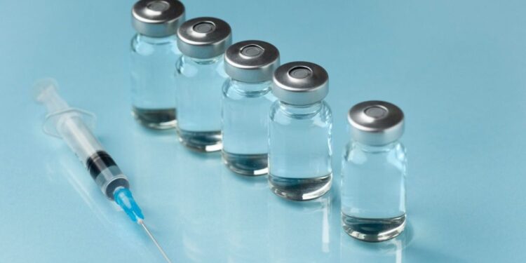 Frascos de medicamento injetável alinhados ao lado de uma seringa sobre superfície azul.