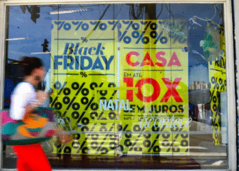 Fachada de loja com vitrines decoradas para Black Friday, adesivos de promoções e pessoa passando em frente