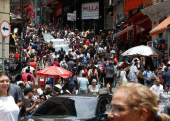 Multidão de pessoas caminhando em uma rua comercial movimentada com várias lojas e ambulantes.