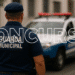 Guarda municipal de costas, vestindo uniforme azul e boné, ao lado de viatura policial branca com luzes vermelhas acesas, em rua urbana com edifícios ao fundo, e texto promocional "CONCURSO GUARDA MUNICIPAL".