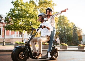Casal usando scooter elétrica com capacetes em via pública representando nova legislação de ciclomotores 2026