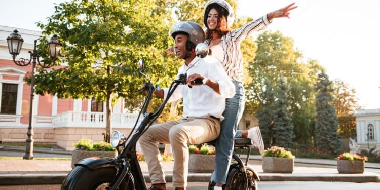 Casal usando scooter elétrica com capacetes em via pública representando nova legislação de ciclomotores 2026