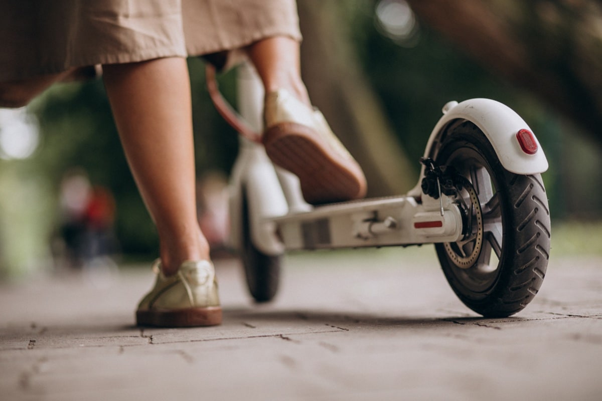 Pessoa usando patinete elétrico na calçada mostrando tipo de veículo autopropelido afetado por novas regras de trânsito.