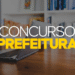 Banner promocional com texto "Concurso Prefeitura" sobre uma mesa de madeira com laptop e estante de livros ao fundo.
