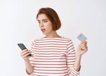 Mulher preocupada olhando celular e cartão após descobrir golpe do SIM Swap