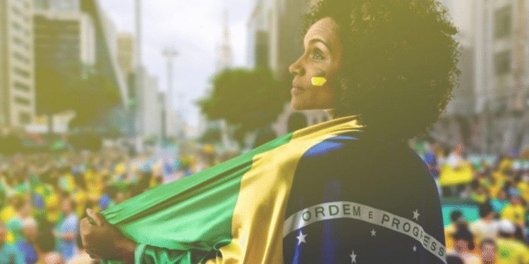 Mulher com rosto pintado, envolta na bandeira do Brasil em manifestação na rua.