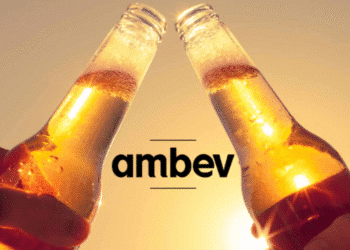Duas garrafas de cerveja sendo brindadas ao pôr do sol com o logotipo da Ambev ao centro.
