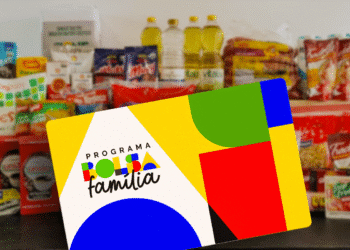 Cartão do Programa Bolsa Família em primeiro plano com fundo desfocado mostrando uma variedade de alimentos básicos (arroz, óleo, café, farinha), simbolizando o auxílio governamental a famílias de baixa renda.