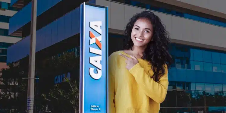 Mulher sorridente apontando para o letreiro da Caixa Econômica Federal em frente a um prédio corporativo.