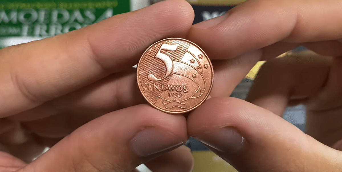 Moeda de cinco centavos sendo segurada próxima à câmera mostrando detalhes de cunhagem rara
