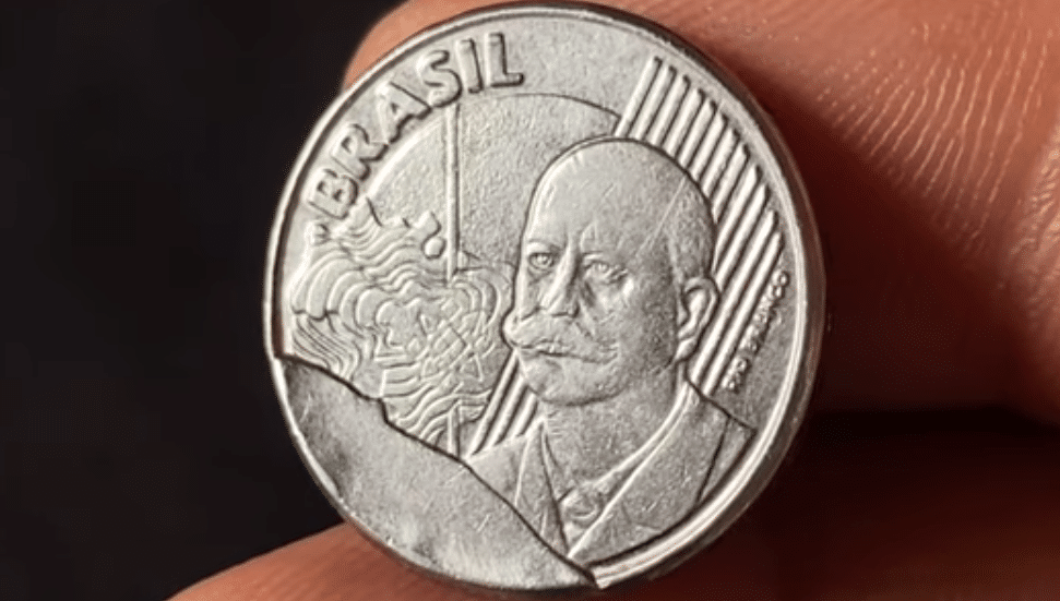 Moeda de 50 centavos de 2002 em close-up, destacando o cunho quebrado vistoso na lateral do busto do Barão do Rio Branco, erro que a torna valiosa.