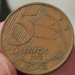 Close-up da moeda brasileira de 5 centavos ano 2002, destacando o número 5, o ano e o defeito de cunho marcado (erro de fabricação)