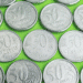 Close-up de diversas moedas de 50 centavos de diferentes anos (incluindo 1994, 2002 e 2016) sobre um fundo verde, representando a procura por anomalias e moedas raras no troco do dia a dia.