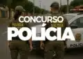 Dois policiais militares em uniforme verde observam a rua ao lado de viatura da polícia