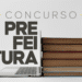 Notebook aberto encostado em pilha de livros com palavra concurso prefeitura ao lado.