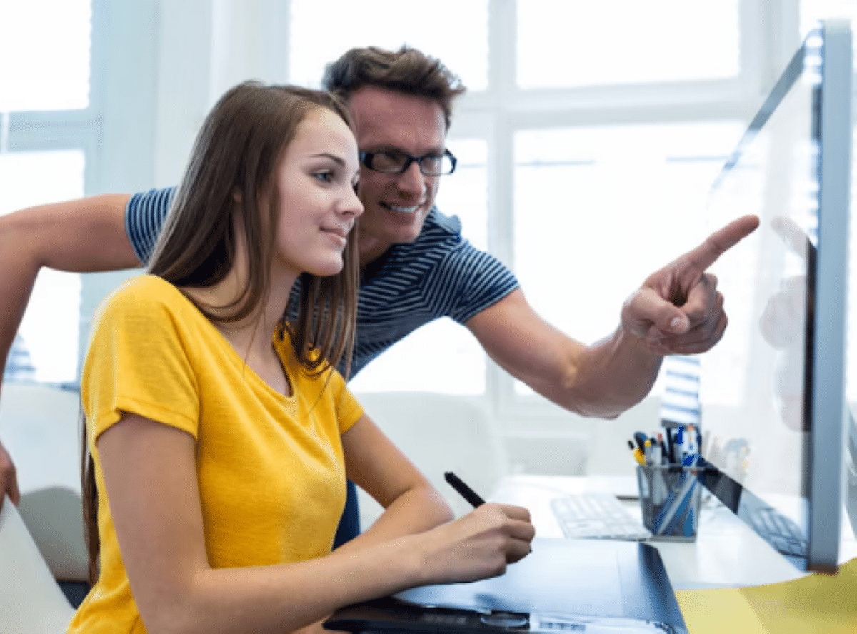 Jovem mulher usando tablet digital com instrutor apontando para a tela do computador
