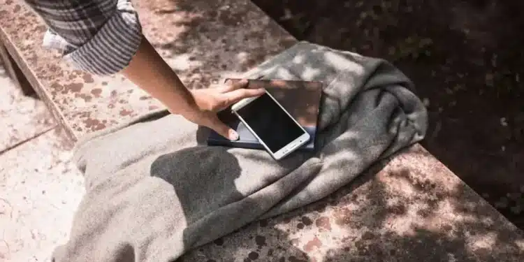Uma mão tocando um smartphone e um caderno sobre um tecido, com sombras projetadas na superfície ao redor.