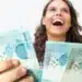 Mulher sorridente segurando notas de 100 reais após receber pagamento.