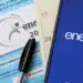 Caderno de provas do Exame Nacional do Ensino Médio (ENEM) com o logo da prova, uma caneta preta e um celular ao lado exibindo o nome "enem" em tela azul.