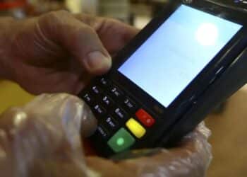 Pessoa utilizando maquininha de cartão de crédito para pagamento, exibindo o teclado numérico e a tela com o valor da transação.