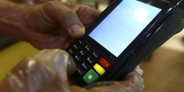 Pessoa utilizando maquininha de cartão de crédito para pagamento, exibindo o teclado numérico e a tela com o valor da transação.