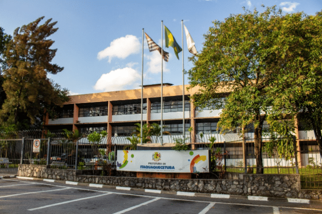 Prefeitura de Itaquaquecetuba–SP encerra inscrições para concurso nesta terça-feira, 25 Fachada da Prefeitura de Itaquaquecetuba–SP com bandeiras hasteadas e área externa arborizada.