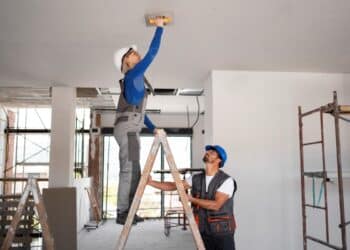 Trabalhadores aplicando acabamento no teto durante reforma residencial.