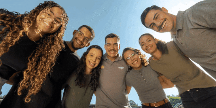 Grupo de jovens aprendizes e colaboradores da Raízen sorrindo em ambiente corporativo.