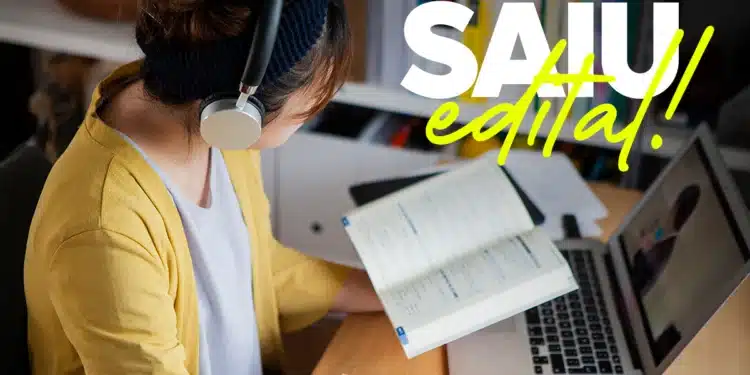 Mulher com fones de ouvido, lendo livro e tomando nota em frente a laptop em ambiente de estudo