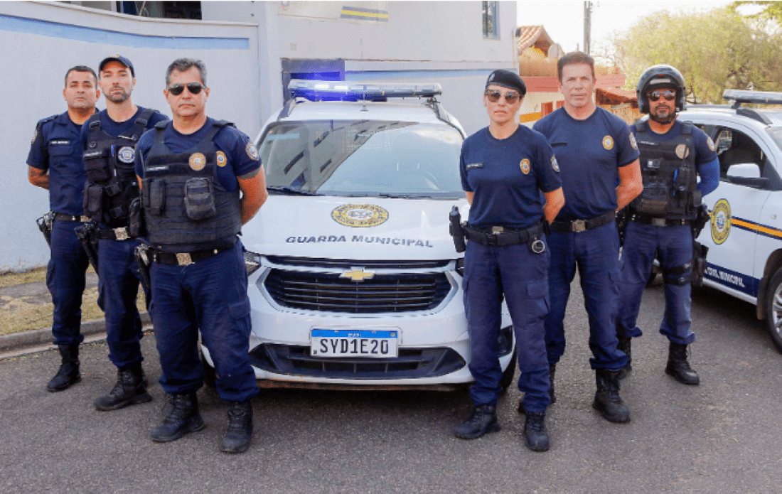 Grupo de agentes da Guarda Municipal de Alfenas–MG posando em frente a viaturas.